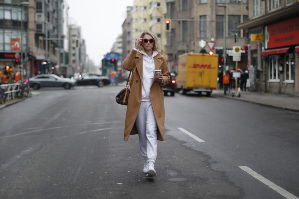 Femme habillée en blanc avec manteau marron marchant dans la rue