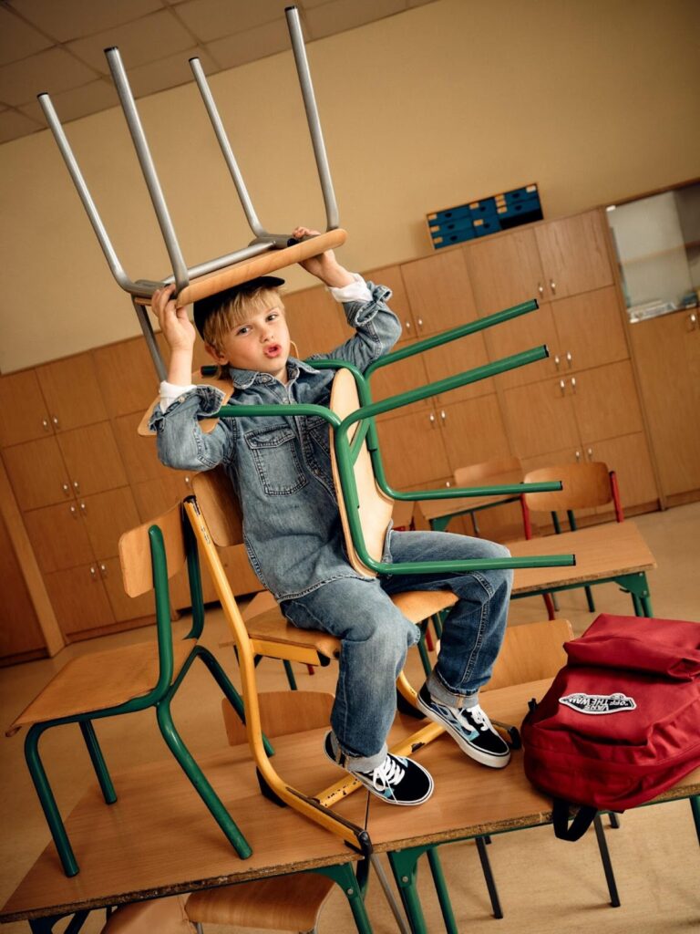 Garçon en look denim assis sur une table dans une salle de classe