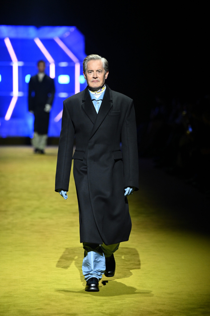 Homme en long manteau noir, pantalon brillant et gants