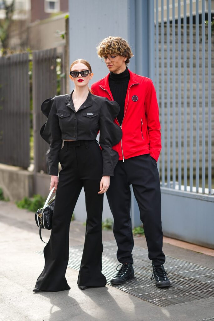 Femme en total look noir et homme en col roulé noir, pantalon noir et veste rouge