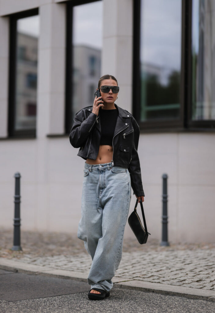 Femme dans une veste perfecto noire, un jean large et un petit sac baguette
