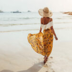 Femme marchant sur la plage avec un chapeau de paille et une robe à motifs légère